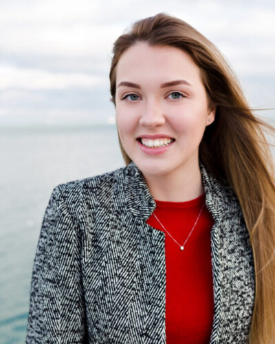 Portrait of smiling pretty girl with flying long hair enjoys good weather and walking by the sea with true happy emotions